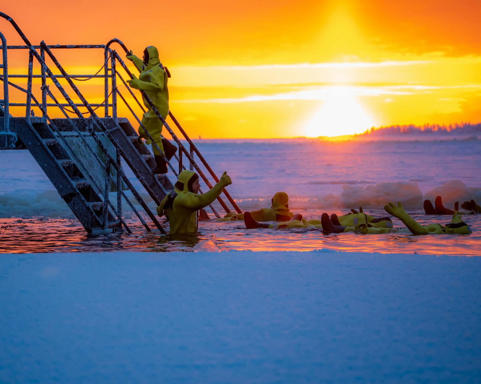 Grupa osób w żółtych strojach morsuje w przerębli o wschodzie słońca
